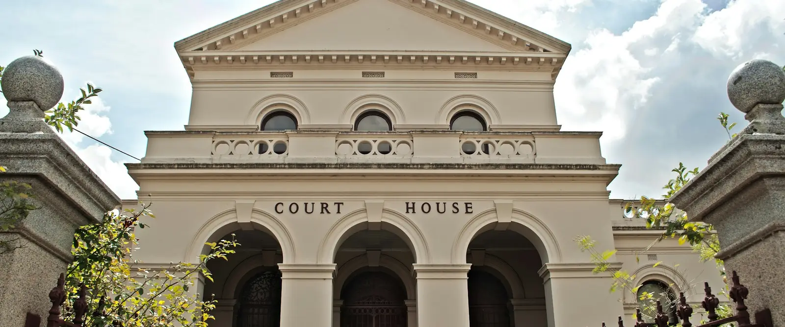 The front of a courthouse with arched entrances, under a partly cloudy sky